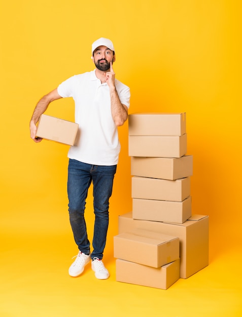 Tiro de cuerpo entero del repartidor entre cajas sobre amarillo aislado Mirando al frente