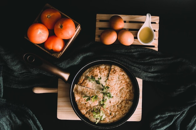 Tiro de alto ângulo de uma omelete em um torrador preto, tomate, ovos frescos e gema de ovo