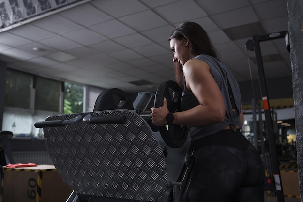 Tiro de ângulo baixo de um fisiculturista feminino colocando pesos na máquina de leg press