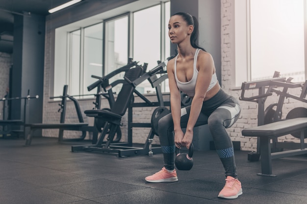 Tiro de ângulo baixo de uma atleta sexy exercitando com kettlebell na Academia