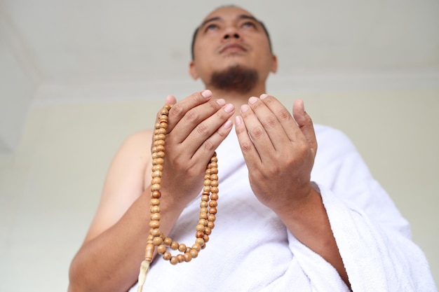 Tiro de ângulo baixo do homem muçulmano asiático vestindo roupas brancas de ihram e rezando enquanto segurava o cordão de oração
