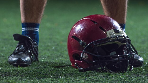 tiro de close-up do jogador de futebol americano e capacete no campo de grama à noite