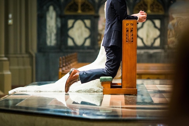 Tiro de foco raso de uma noiva e um noivo ajoelhados em um genuflexório de oração dentro da igreja