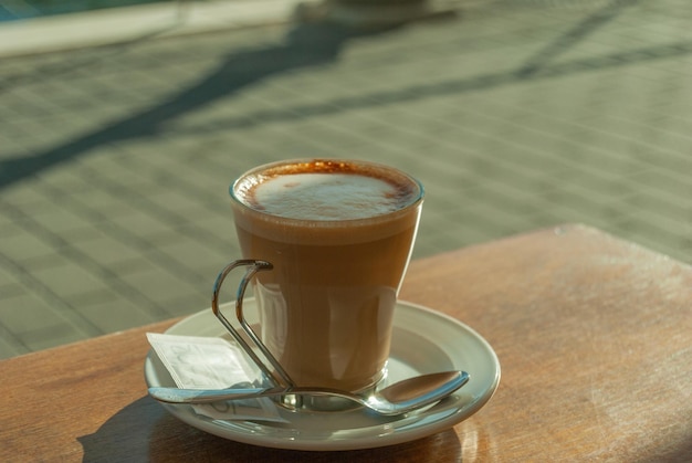 Tiro de foco seletivo de café cortado com leite em um copo de vidro na mesa de um café ao ar livre