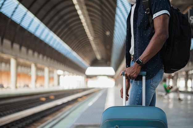 Tiro de homem negro esperando o trem Ele está segurando uma mala azul