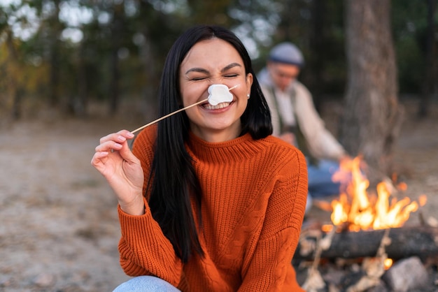 Tiro de jovem alegre rindo alto enquanto assava marshmallows sobre o fogo. mulher feliz segurando uma vara com marshmallow perto do rosto