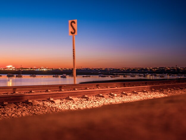 Tiro de longa exposição da ferrovia de faros no pôr do sol e no mar.