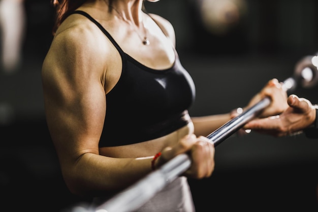 Tiro de uma mulher musculosa irreconhecível malhando no treinamento duro no ginásio. Ela está bombeando o músculo do bíceps com peso pesado.