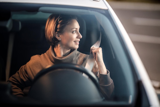 Foto tiro de uma mulher sorridente afivelando o cinto de segurança enquanto está sentado em seu carro.