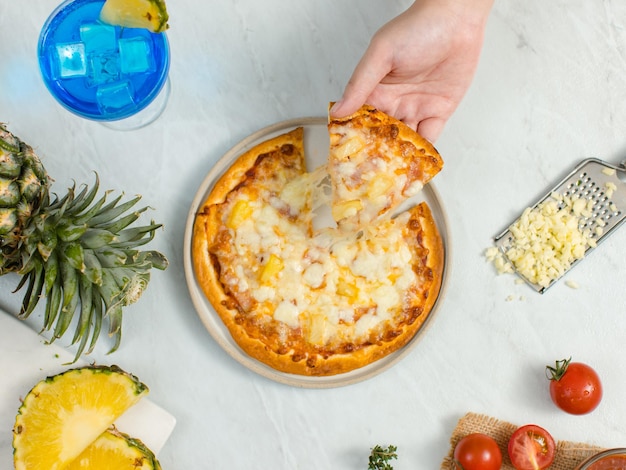 Tiro de vista superior da mão humana desconhecida irreconhecível, pegando um pedaço de deliciosa crosta italiana tradicional havaiana fina crocante presunto e pizza de abacaxi estendendo o queijo da mesa