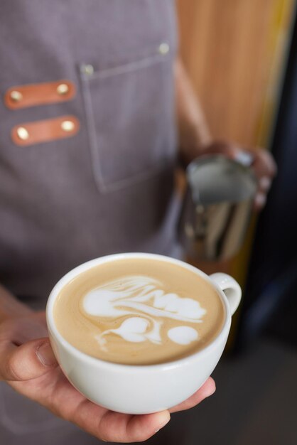 Tiro de vista superior do barista profissional derramando leite da jarra em uma xícara de café café sendo preparado por um barista Foco nas mãos segurando a xícara de café