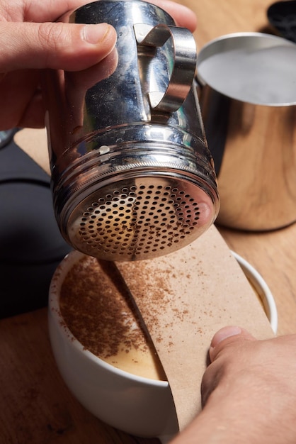 Tiro de vista superior do barista profissional derramando leite da jarra em uma xícara de café café sendo preparado por um barista Foco nas mãos segurando a xícara de café