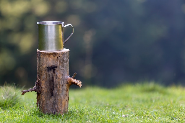 Tiro do close-up, caneca grande e brilhante da lata no tronco de árvore isolado ao ar livre na floresta gramínea ensolarada do verão