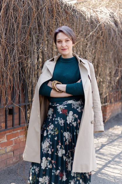 Tiro do retrato de uma mulher atraente e elegante atalho, garota caminha ao ar livre da cidade. imagem elegante, moderna e feminina, estilo. menina com uma capa ou casaco bege e um vestido verde