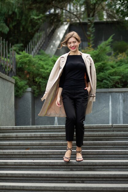 Tiro de estilo de vida de una joven alegre con labios rojos y pelo corto y rizado viste un traje moderno bajando las escaleras