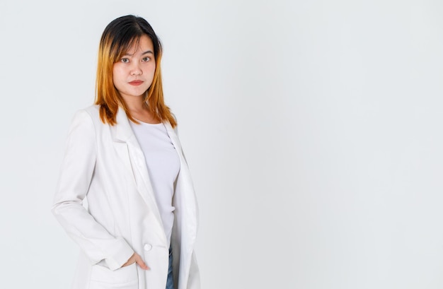 Tiro del estudio del retrato del modelo femenino del pelo teñido feliz hermoso urbano de moda asiático de la moda en la camiseta del traje largo casual y los pantalones vaqueros del dril de algodón que se colocan sonriendo mirar la cámara que presenta en el fondo blanco.