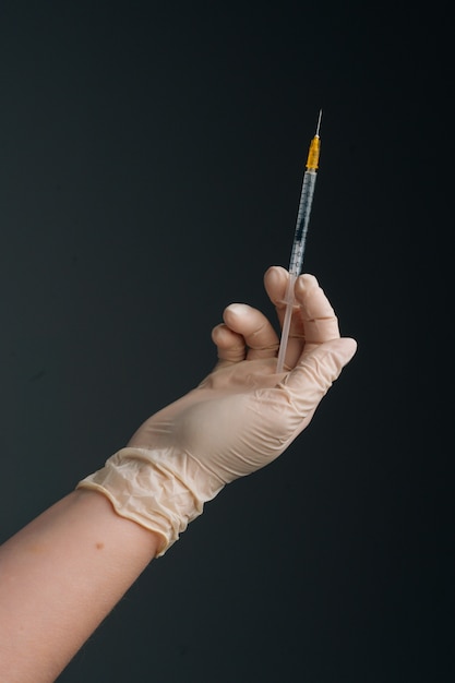 Tiro de estudio vertical de trabajador de la salud con guantes de protección está sosteniendo la jeringa, primer plano. Primer plano de una enfermera irreconocible con guantes de látex blancos sosteniendo una jeringa sobre fondo negro aislado.