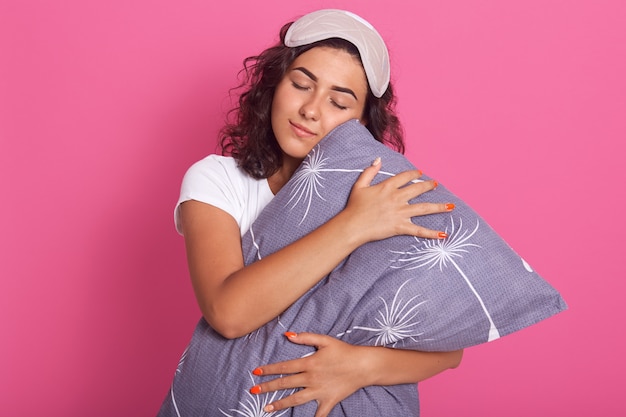 Tiro horizontal de bastante joven mujer caucásica abraza almohada suave gris