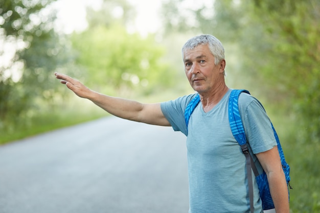 Foto tiro horizontal de bonito enrugado masculino carona na estrada