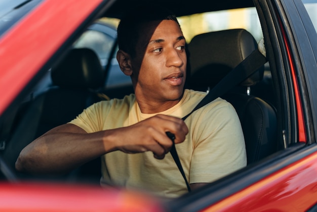 Tiro horizontal do jovem multirracial apertando os cintos de segurança enquanto está sentado e se preparando para dirigir o carro na estrada. conceito de transporte