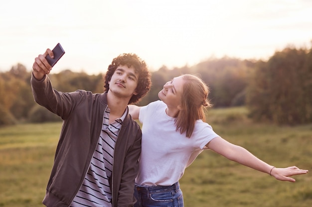 Tiro horizontal dos melhores amigos positivos posar no telefone inteligente para fazer selfie