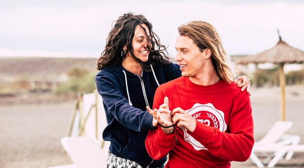 Tiro horizontal de la feliz pareja joven en la playa Hombre y mujer jóvenes riendo cerca del entorno del sol del paraguas y disfrutando juntos de las vacaciones y la actividad de ocio al aire libre