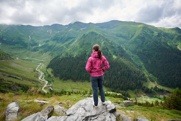 Tiro integral de una excursionista femenina de pie en la cima de una montaña mirando a su alrededor