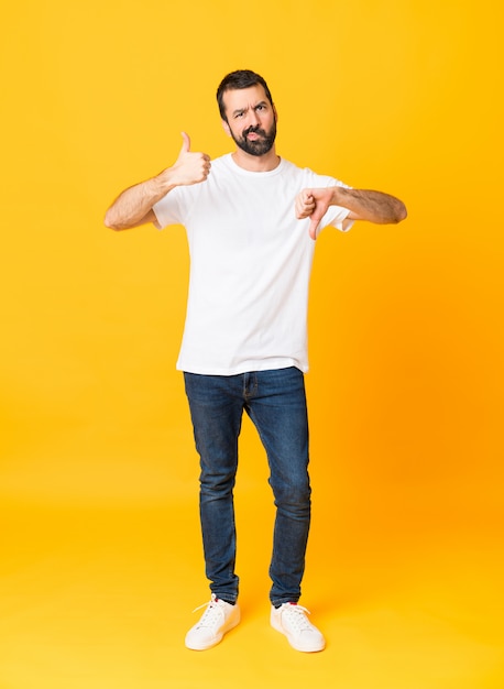 Tiro integral del hombre con barba sobre amarillo aislado haciendo buena-mala señal. Indeciso entre sí o no