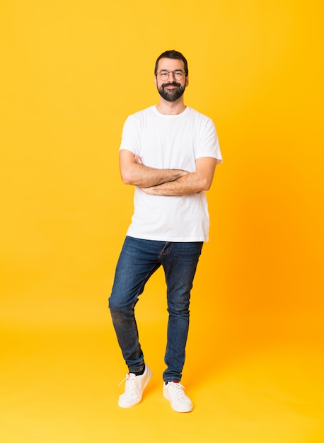 Tiro integral del hombre con barba sobre pared amarilla aislada con gafas y feliz