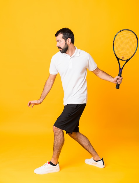 Tiro integral del hombre jugando tenis sobre amarillo aislado