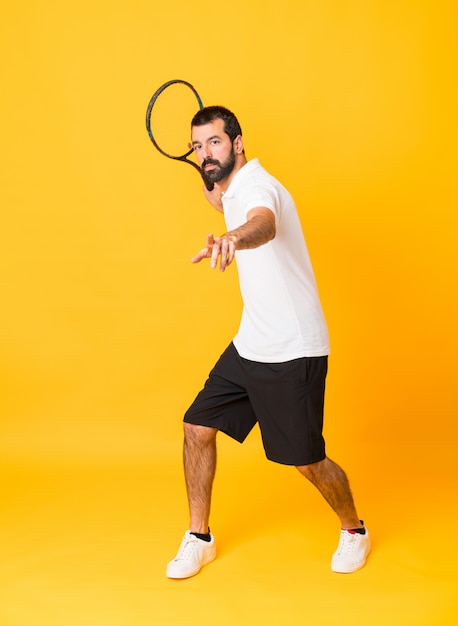 Tiro integral del hombre jugando tenis sobre amarillo aislado