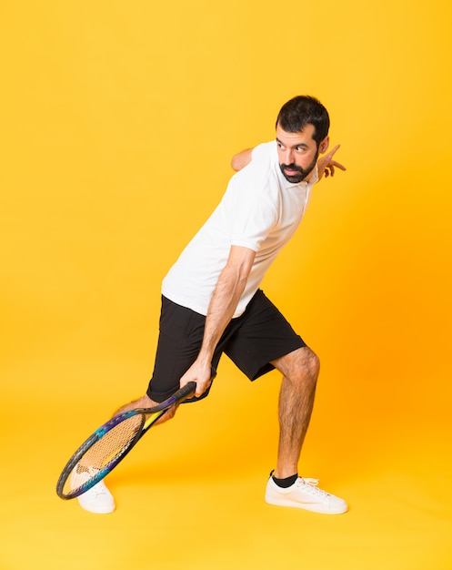 Tiro integral del hombre jugando tenis sobre amarillo aislado