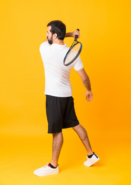 Tiro integral del hombre jugando tenis sobre amarillo