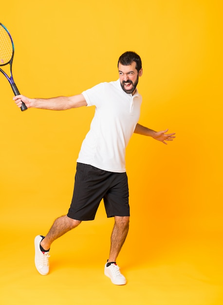 Tiro integral del hombre jugando tenis sobre fondo amarillo aislado