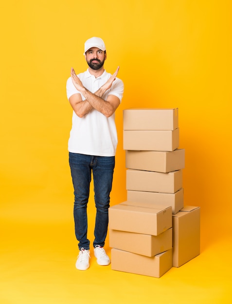 Foto tiro integral del repartidor entre cajas sobre amarillo aislado sin hacer ningún gesto