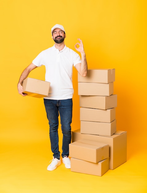 Tiro integral del repartidor entre cajas sobre amarillo aislado en pose zen