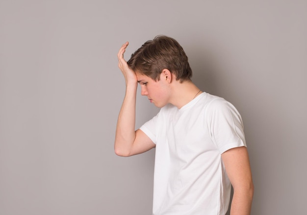 Tiro interno de estudante estressado desapontado em camiseta branca fazendo facepalm com a mão