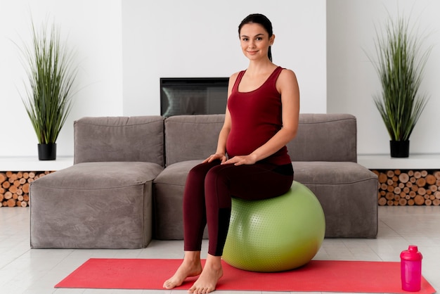 Foto tiro largo mujer embarazada sentada en una pelota de fitness