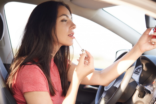 Tiro lateral de la bella mujer morena aplica lápiz labial