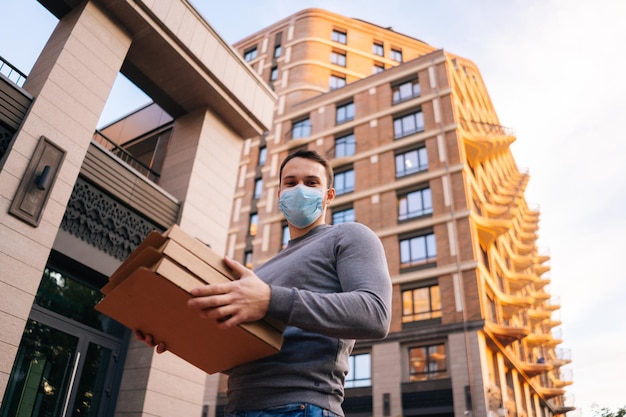 Tiro lowangle do entregador usando máscara de proteção médica segurando caixas de papelão com pizza quente