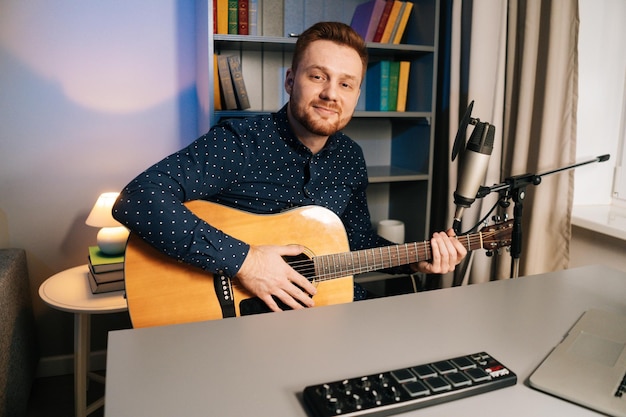 Tiro médio do homem bonito cantor guitarrista toca violão gravando música cantando usando suporte de microfone profissional em estúdio doméstico