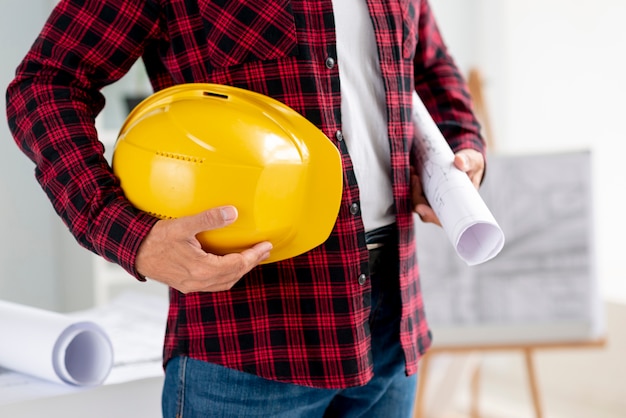 Tiro medio hombre sosteniendo planos arquitectónicos y casco de seguridad