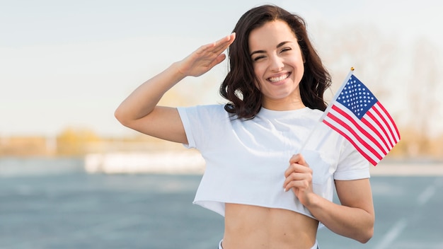 Tiro medio mujer mano saludando y sosteniendo la bandera de Estados Unidos