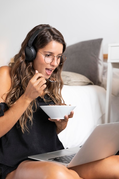 Tiro medio mujer sentada en el suelo comiendo y mirando portátil