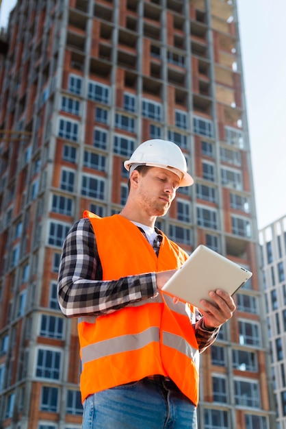 Tiro médio, vista baixa ângulo, engenheiro construção, olhar, tablete