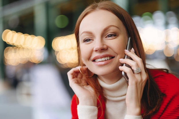 Tiro na cabeça de uma jovem atraente com expressão facial feliz fala via celular tem cabelo castanho feliz em ouvir notícias tem tempo livre fundo desfocado com espaço de cópia para sua promoção