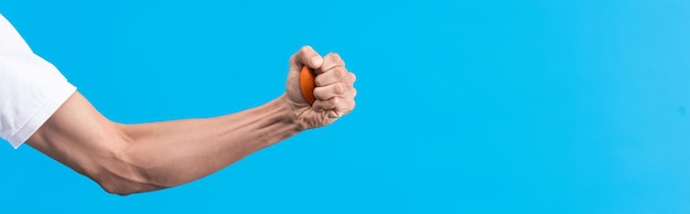 Tiro panorâmico de homem irritado apertando bola de estresse na mão isolada em azul