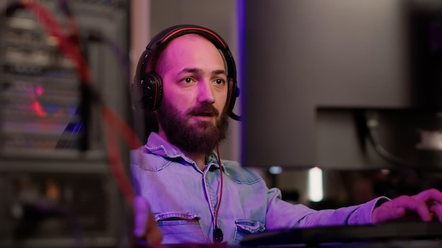 Foto tiro portátil do jogador com jogabilidade de streaming de fone de ouvido gritando após vencer o jogo multiplayer online na configuração do pc para jogos. homem caucasiano comemorando a vitória na competição de computador online com amigos.