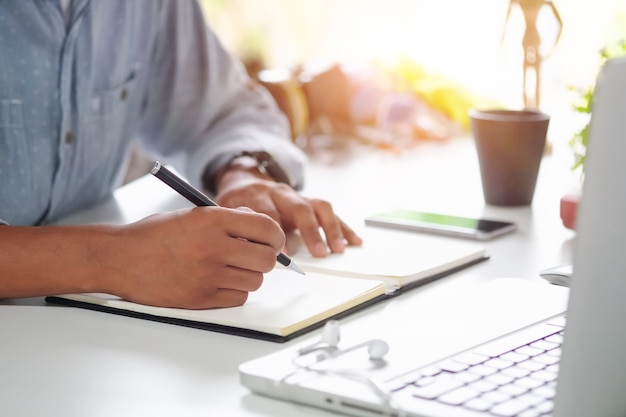 Tiro recortada un hombre escribiendo en un cuaderno sobre el lugar de trabajo.