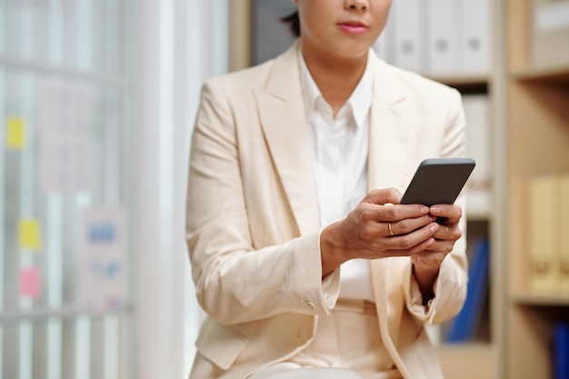 Tiro recortado da jovem empresária elegante em trajes formais usando smartphone